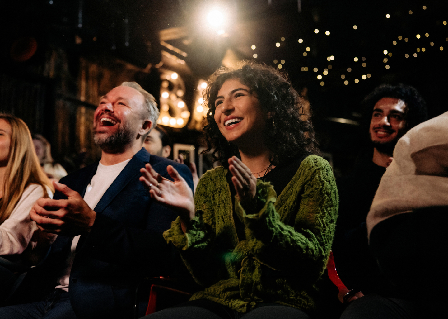 A couple seated in a theater, applauding a performance