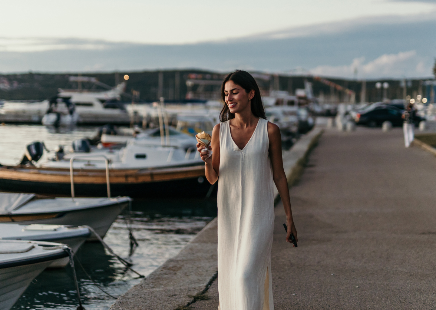 A woman enjoying an ice cream cone as she takes an evening walk along a harbor